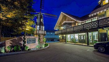 A nighttime view of a charming building with a windmill and lit-up roofline, and a sign that reads 