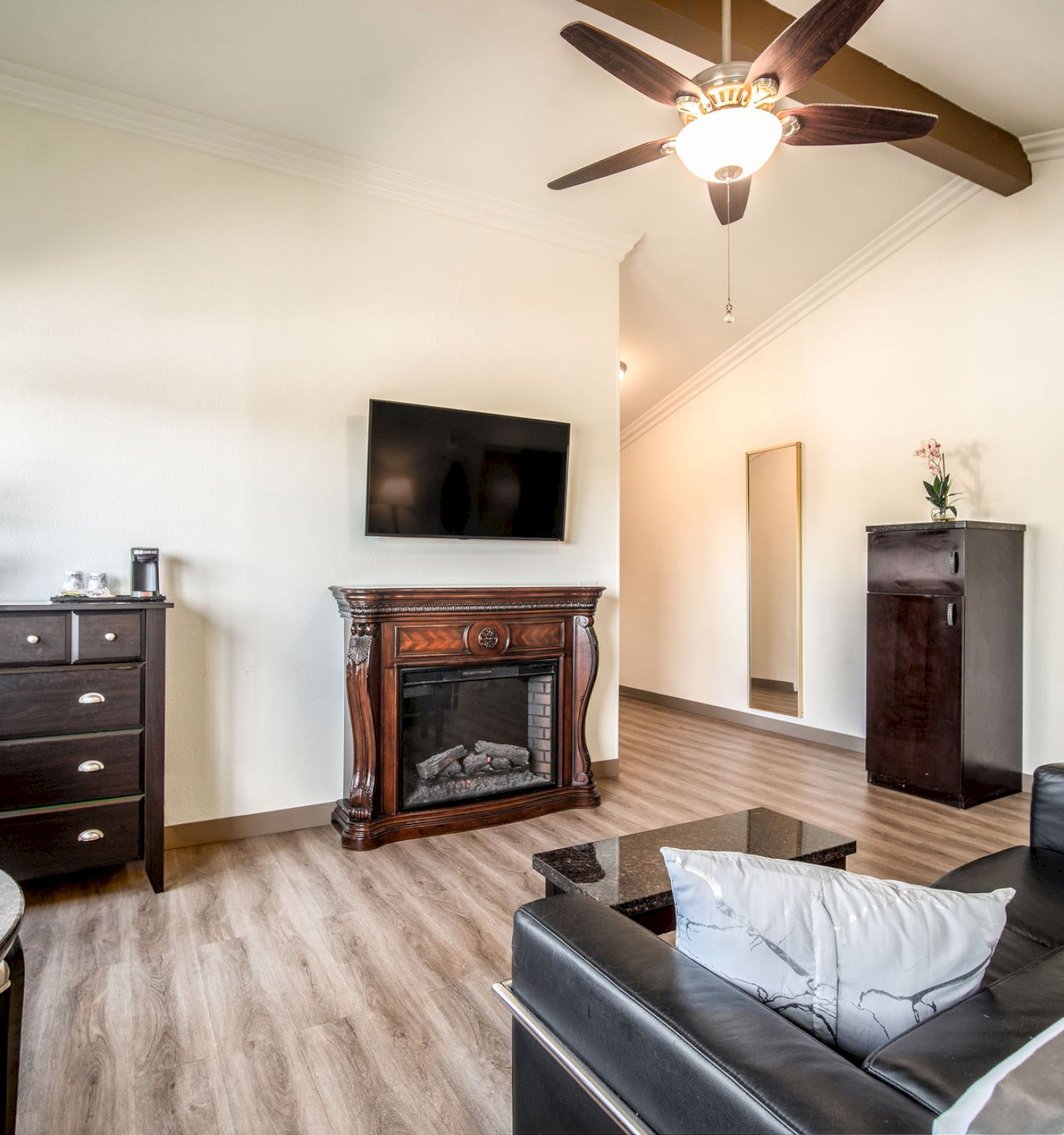 A modern living room with a sleek sofa, flat-screen TV, fireplace, furniture, ceiling fan, and framed artworks on a hardwood floor.