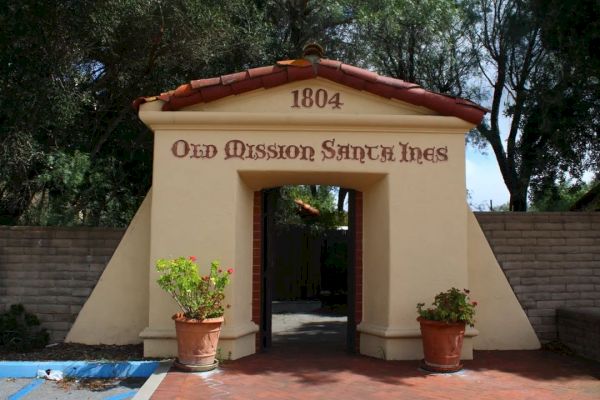 The image shows the entrance to Old Mission Santa Ines, with the year 1804 inscribed at the top and two potted plants beside the doorway.