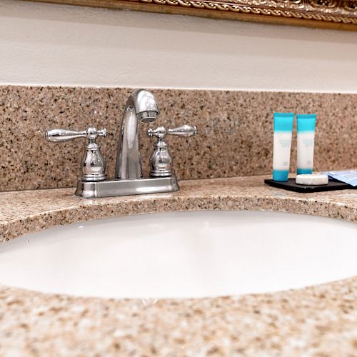 A bathroom sink with a granite countertop, faucet, and neatly arranged toiletries including two tubes and a soap bar on a tray.