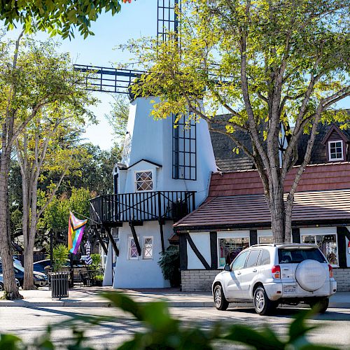 This image shows a quaint building with a windmill, trees, cars, and a rainbow flag on a sunny day, ending the sentence.