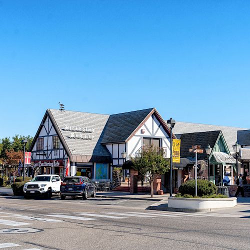 The image shows a street lined with quaint, European-style buildings with timber framing, cars, and bright blue skies, ending the sentence.