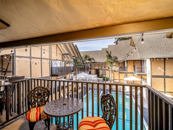 A cozy balcony with ornate table and chairs overlooks a swimming pool in a courtyard of a charming, rustic-style building.
