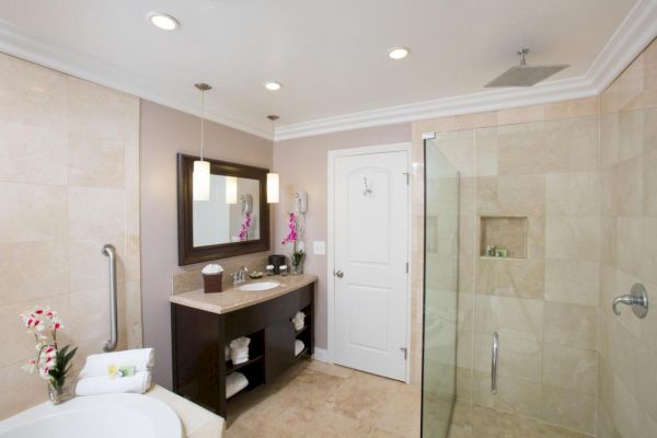 A modern bathroom with a large mirror, dual sinks, and a glass-enclosed shower. There are fresh flowers and neatly folded towels for decor.