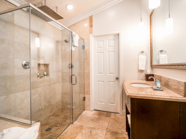 This image shows a modern bathroom with a glass-enclosed shower, a vanity with a sink and mirror, and minimalistic decor in neutral tones.