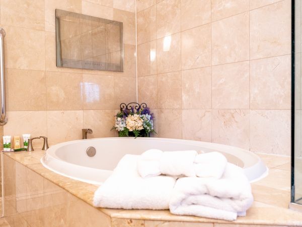 A luxurious bathroom with a marble bathtub, fluffy towels, toiletries, and a bouquet of flowers. The space is well-lit and elegant.