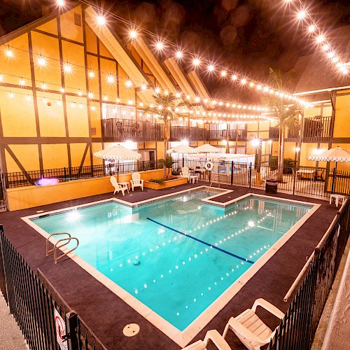 The image features a lit-up swimming pool area surrounded by a fence, with string lights above and lounge chairs and umbrellas on the deck.